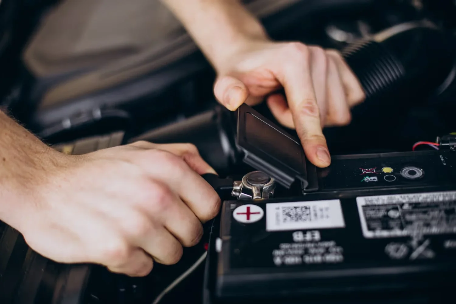 Person's hands connecting a car battery terminal under the hood.