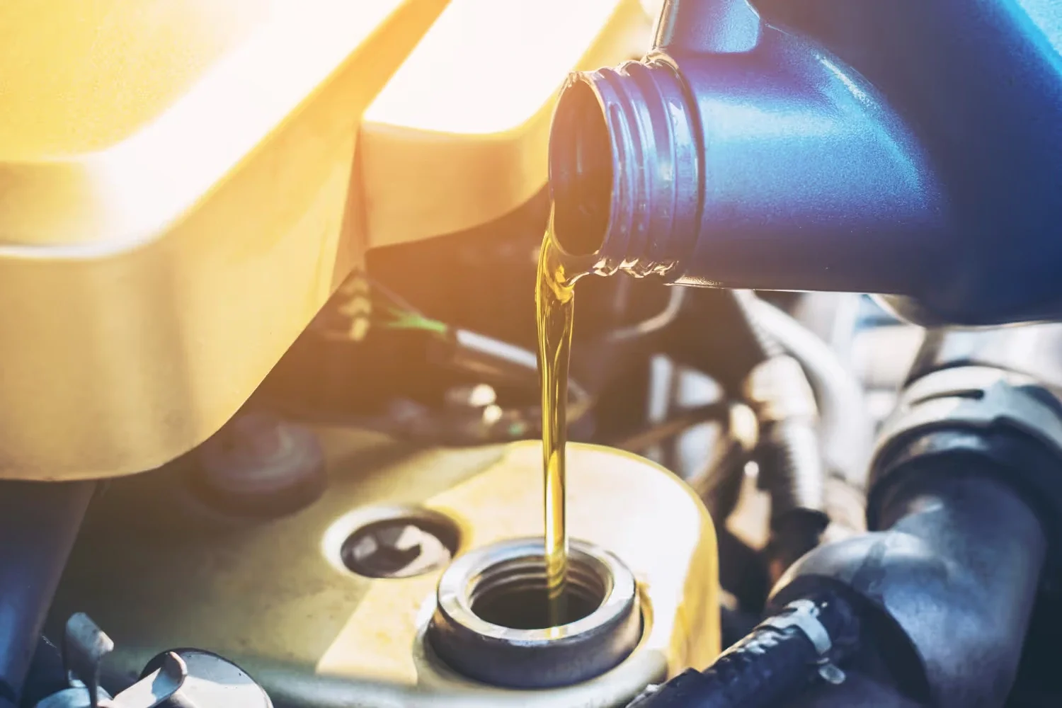 Pouring golden motor oil from a blue bottle into a car engine.