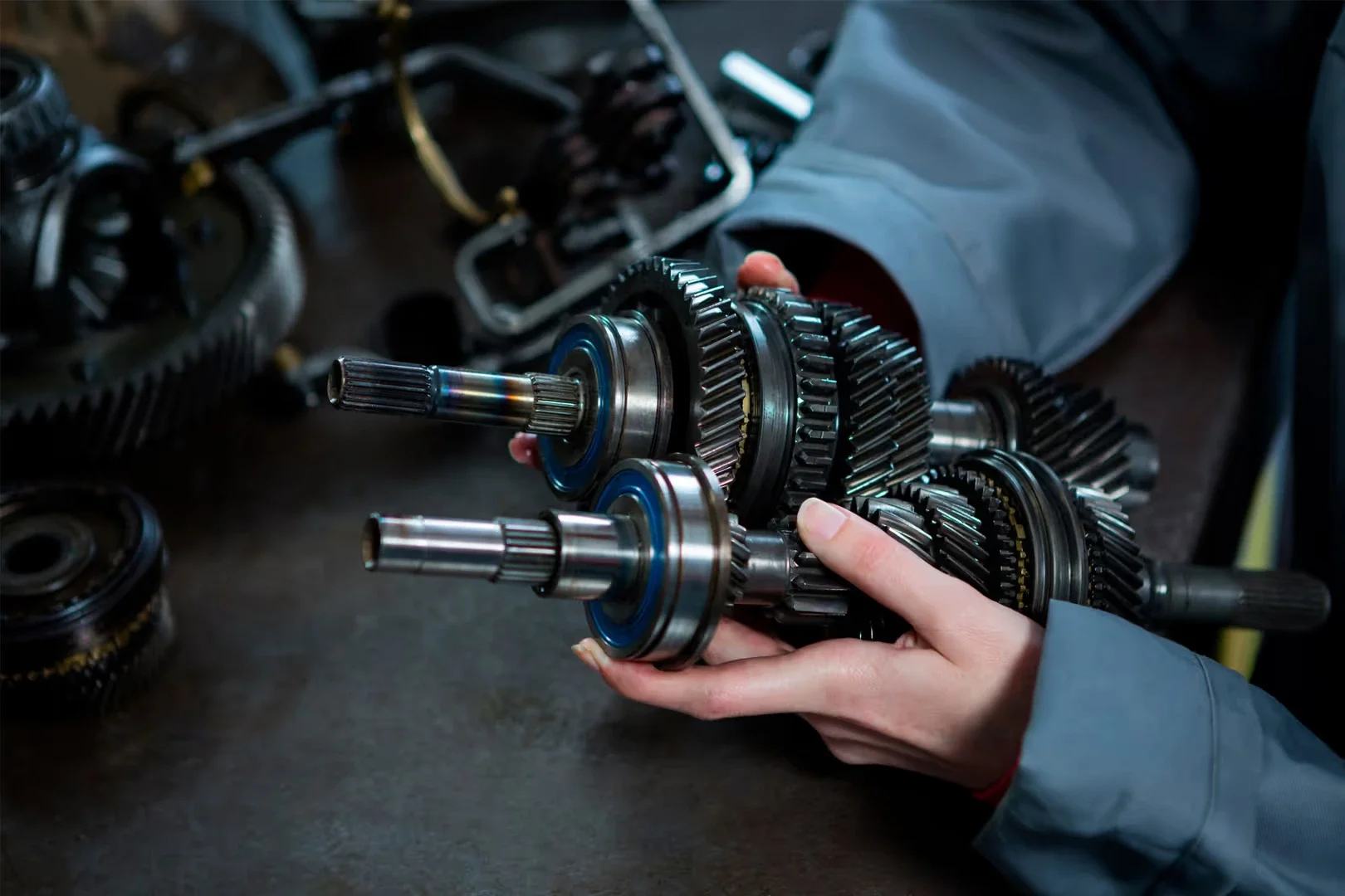 Hands in gray uniform holding two transmission shafts with gears and bearings.